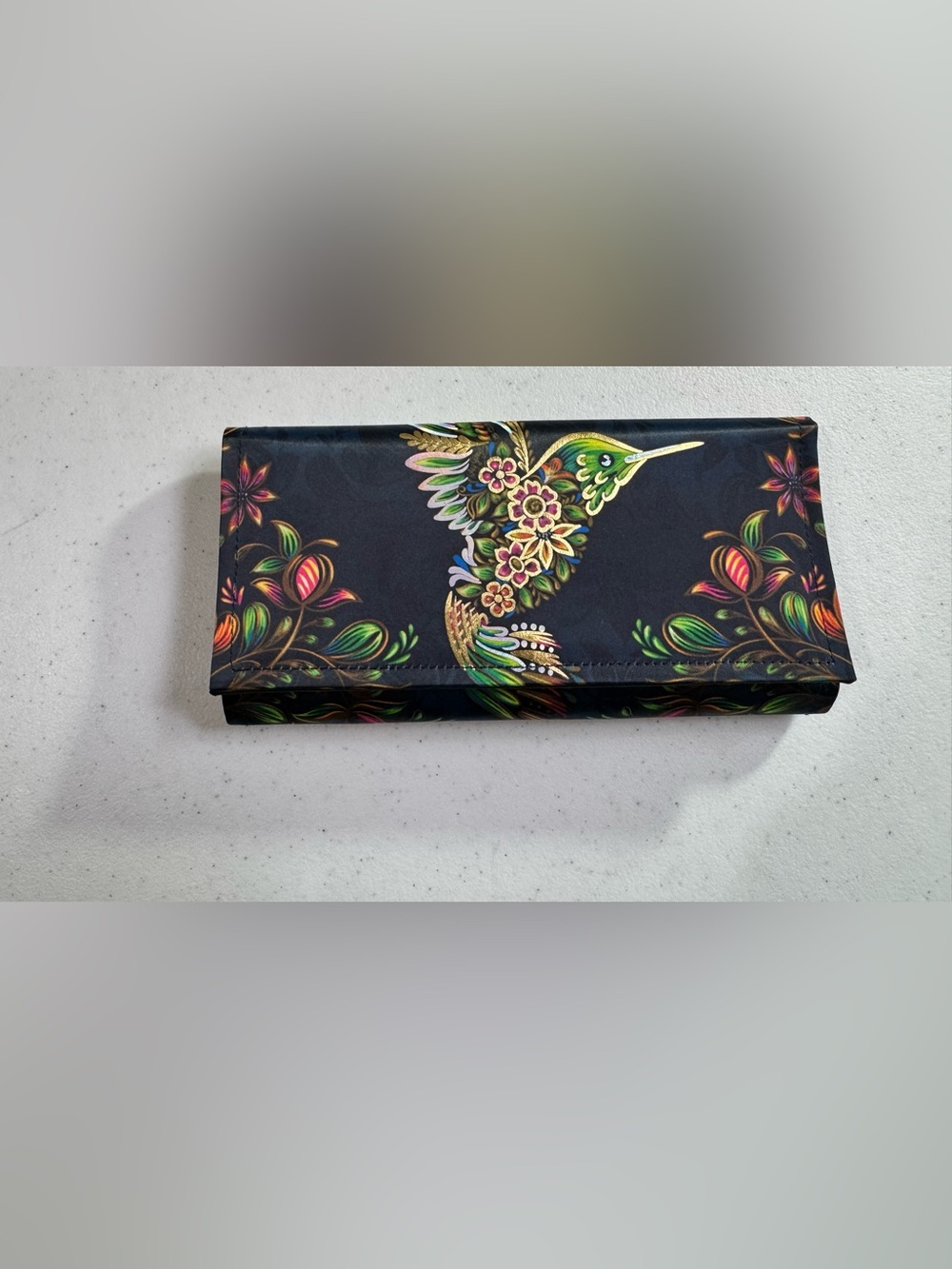 Ay Guey wallet features a vibrant hummingbird and floral artwork/Black 8X4 in.